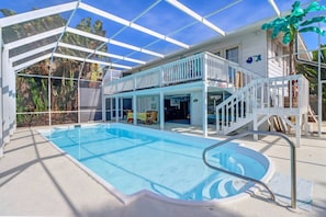 Uma área de piscina com piscina azul cristalina, um deck coberto e uma escadaria que leva a um segundo andar.