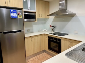 Kitchen features a stainless steel refrigerator, microwave, and induction cooktop, along with light wood cabinetry and a white countertop.