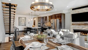 Een moderne keuken met roestvrijstalen apparatuur, een eethoek met een houten tafel gedekt voor vier personen, en een open haard.