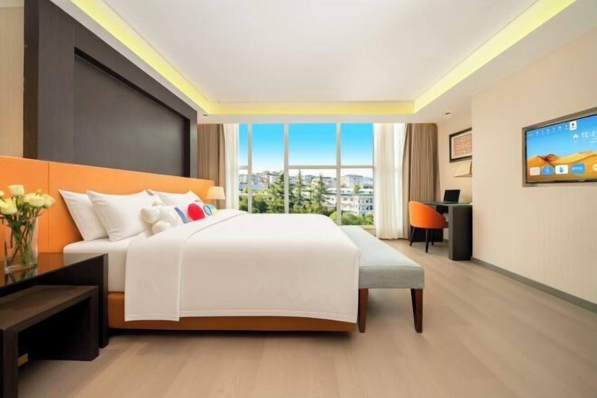 A modern hotel room with a large bed, a desk, a chair, and a TV on the wall.