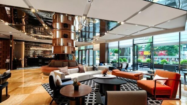 A modern lobby with a central seating area, a staircase, and large windows offering a view of the outdoors. - New Joy Hotel (Internatial Trade Spring Department Store Shopping) (Zunyi)