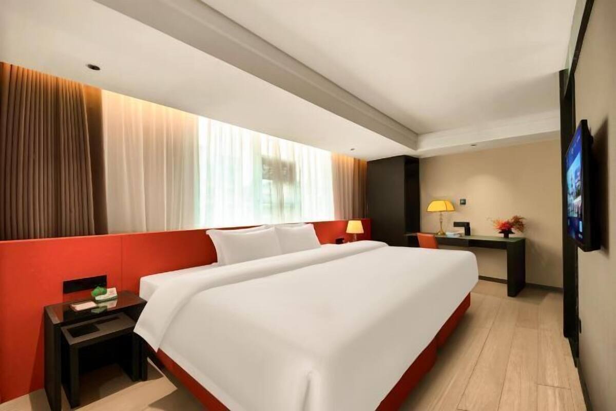 A hotel room with a large bed, a desk, a chair, a TV, and a window with curtains.