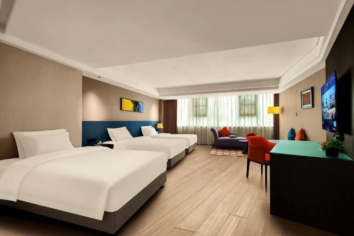 A hotel room with two beds, a desk, a chair, a TV, and a window with curtains.