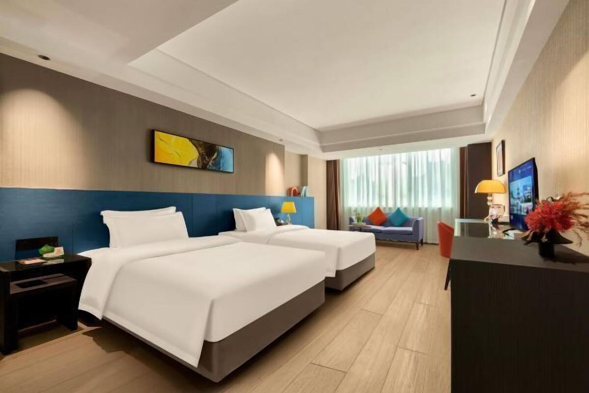 A hotel room with two beds, a desk, a chair, a TV, and a window with curtains.