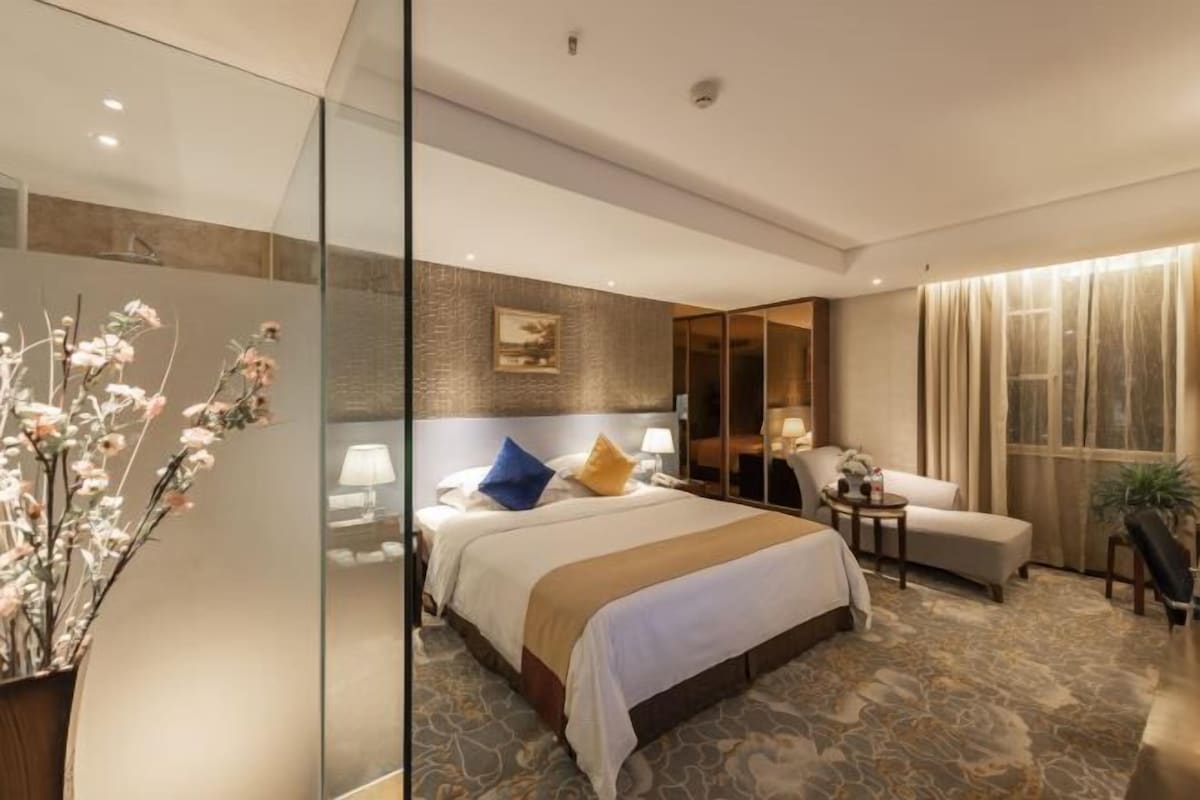 A modern hotel room with a large bed, a sitting area, and a glass partition.