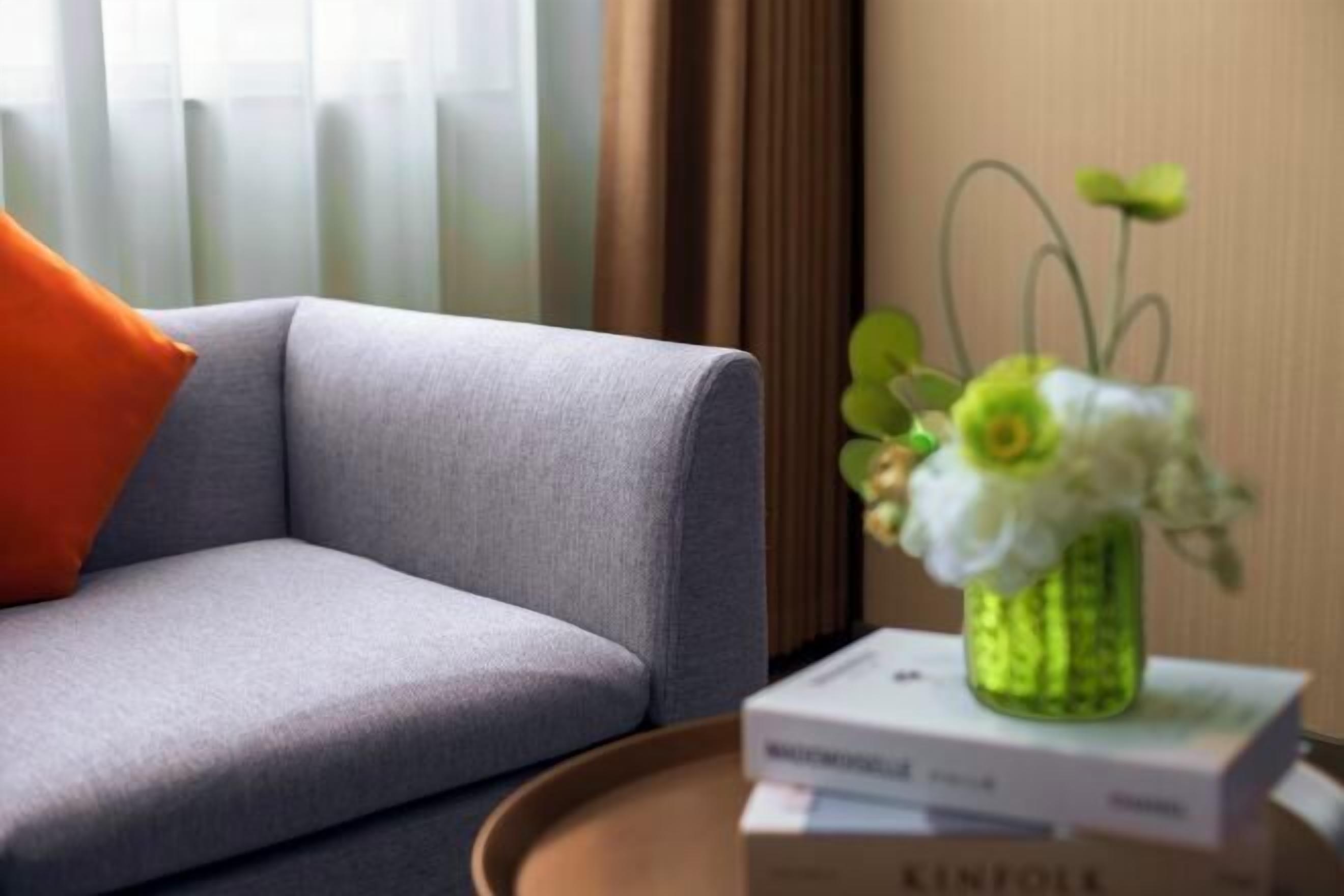 Un canapé gris avec un coussin orange, une petite table sur laquelle est posé un vase vert contenant des fleurs blanches, et un livre intitulé « KINFOLK ».