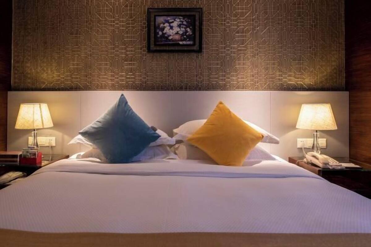 A hotel room with a large bed, two bedside lamps, a framed picture on the wall, and a patterned wallpaper.