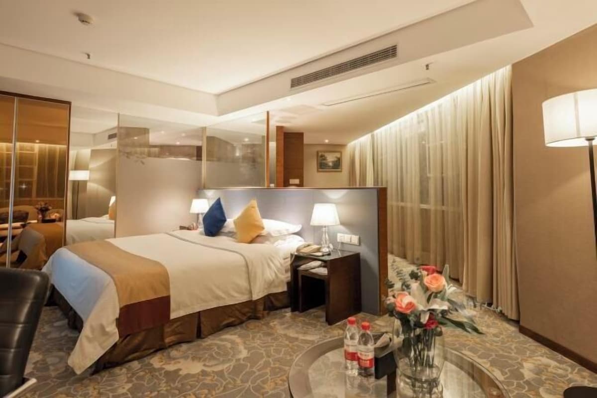 A hotel room with a bed, bedside tables, a mirror, a lamp, a vase with flowers, and a chair.