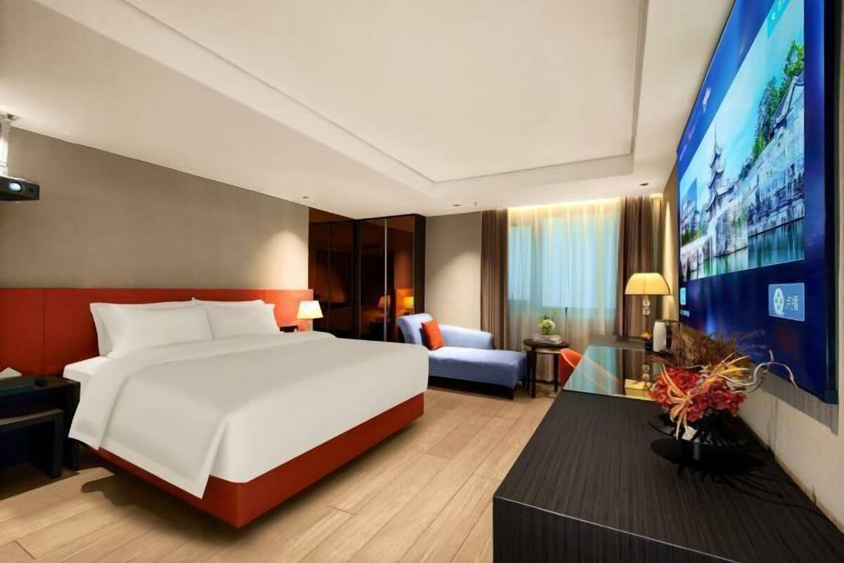 A hotel room with a large bed, a desk, a chair, a TV, and a window with curtains.
