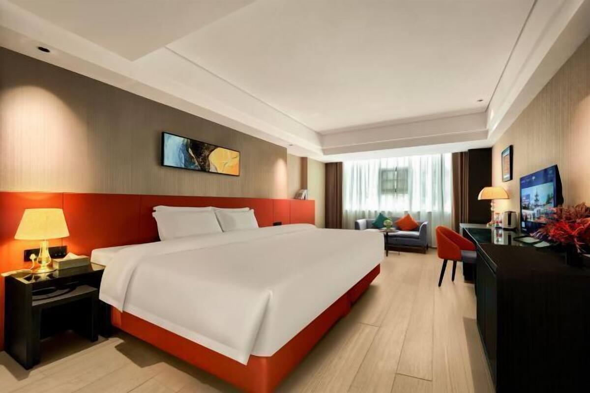 A modern hotel room with a large bed, a desk, a chair, and a television.