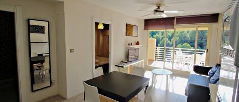 A modern living room with a dining table, chairs, a sofa, and a balcony with a view.