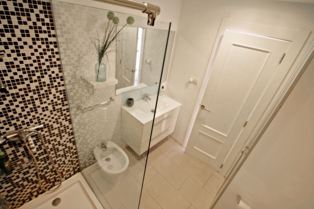 Un bany modern amb una dutxa amb envàs de vidre, un lavabo blanc i un respatller revestit de rajoles.