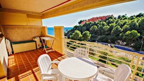 Een balkon met een tafel en stoelen, met uitzicht op een kustgebied met bomen en gebouwen.