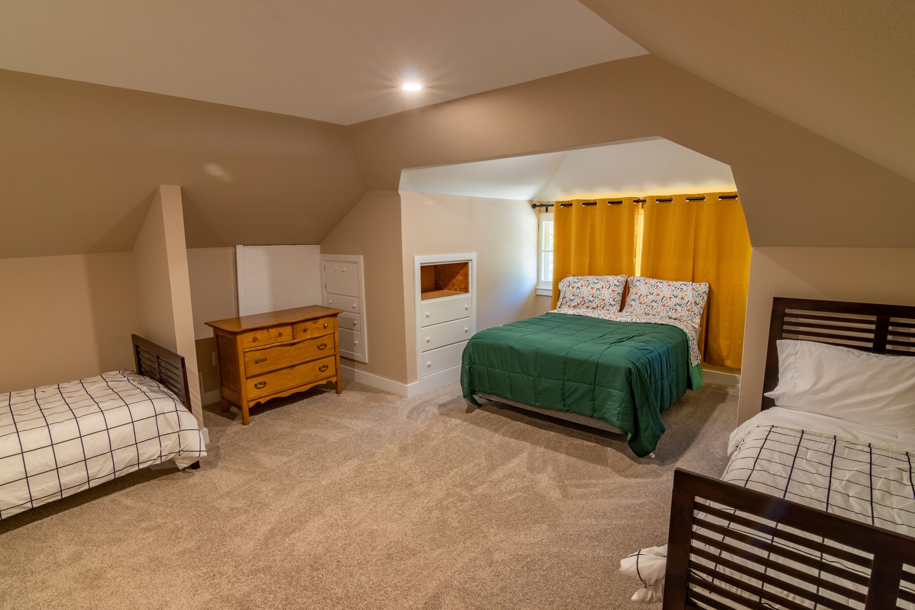 A bedroom with two single beds, a wooden dresser, a nightstand, and a window with yellow curtains.