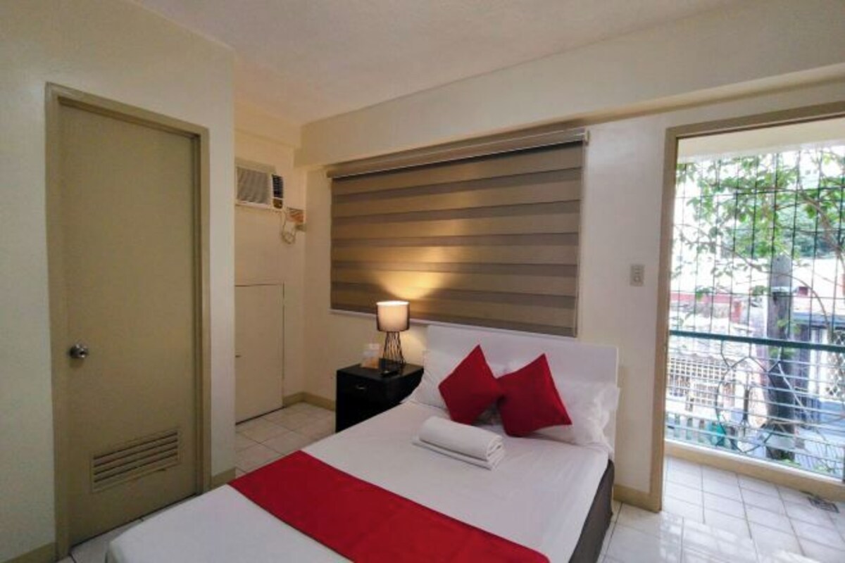 Hotelkamer met een bed, nachtkastje met lamp, raam met zonwering en een deur.