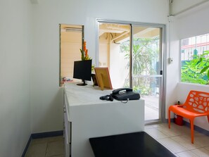 A reception desk with a computer monitor, telephone, and a small plant. There is a sliding glass door leading to an outdoor area with greenery. - OYO 840 Orangenest Apartelle (Manila)