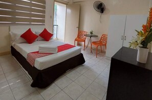 Une chambre d’hôtel comprenant un lit, deux chaises, une petite table, un ventilateur et un placard.