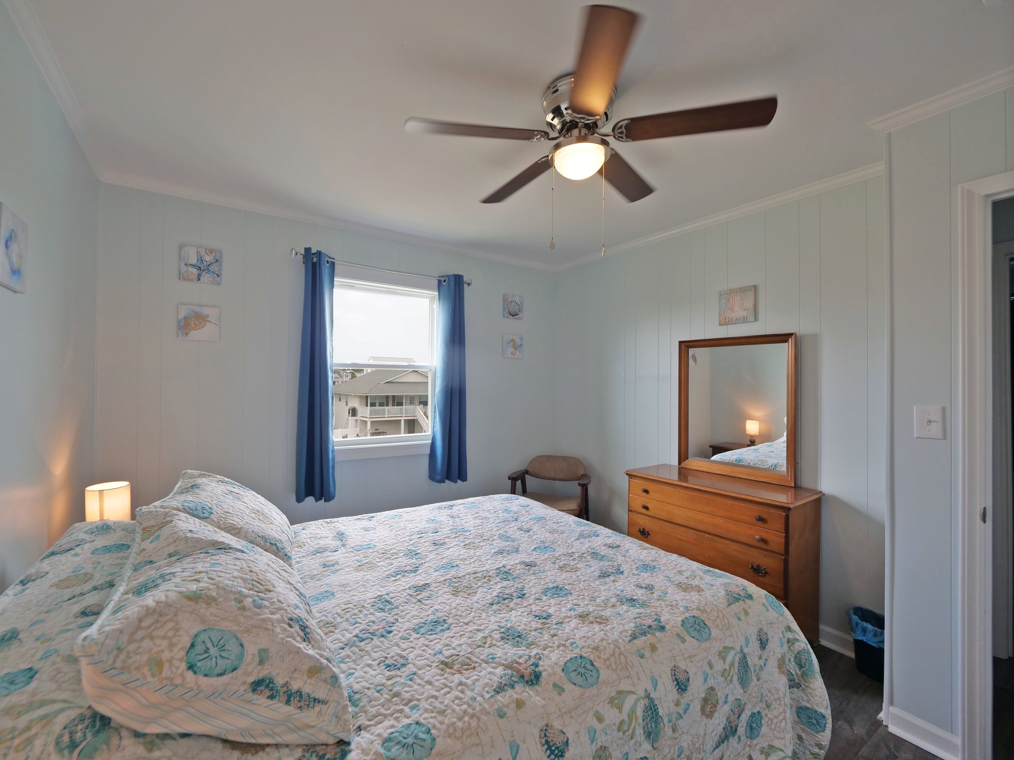 A bedroom with a bed, a dresser, a ceiling fan, a window with curtains, and a mirror.