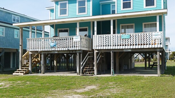 A two-story building with a balcony on the ground floor and a covered porch. - "SeaQuest East" -2nd Row Pet Friendly Duplex, 4 Bedrooms / 3 Bathrooms (Holden Beach)