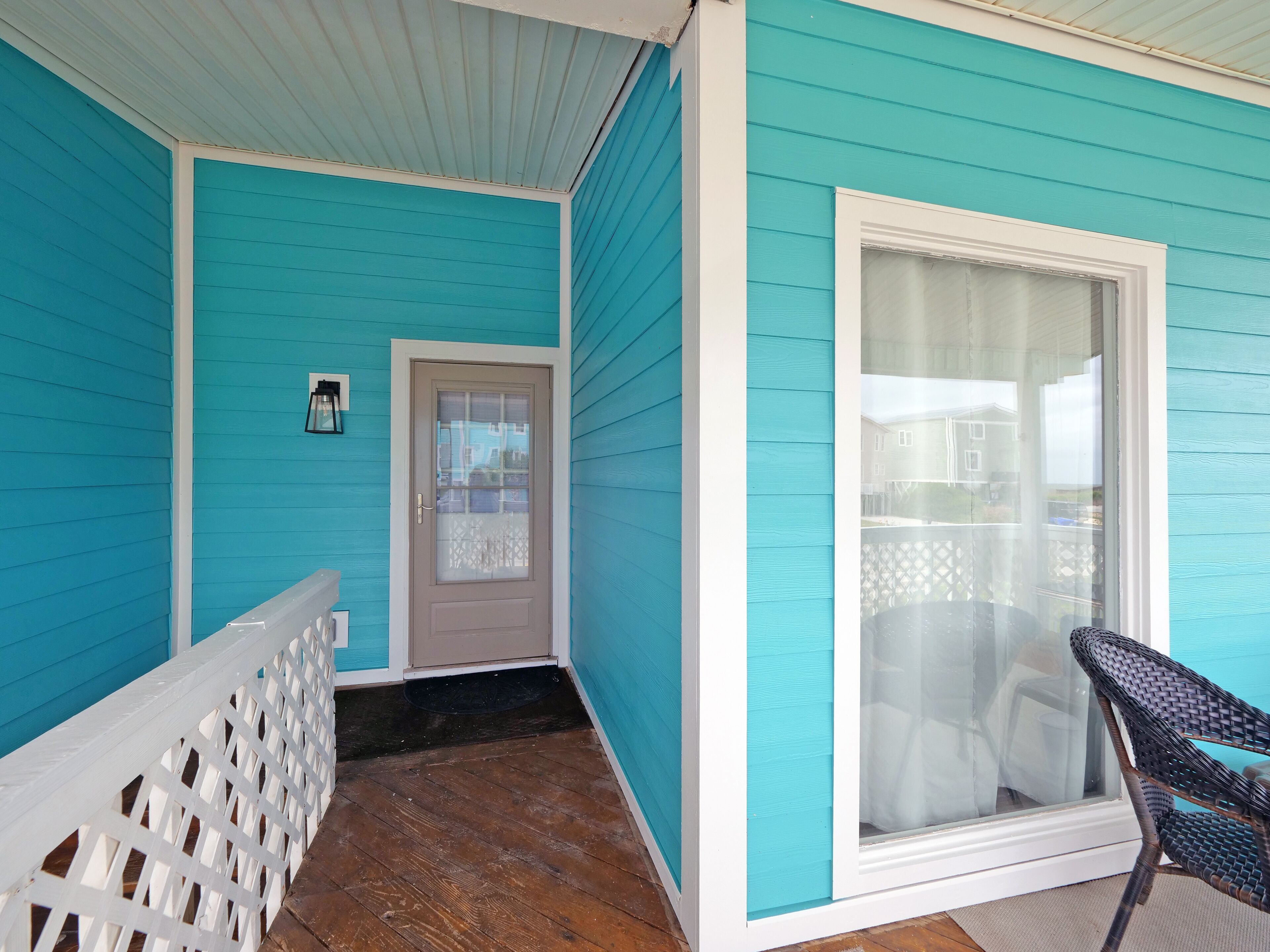 A covered porch with a wooden floor, a white railing, and a door with frosted glass.