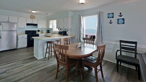 A compact kitchen with white cabinets, a central island, and a dining area with wooden chairs. - "SeaQuest East" -2nd Row Pet Friendly Duplex, 4 Bedrooms / 3 Bathrooms (Holden Beach)