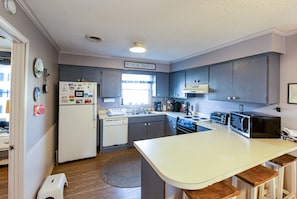 Et kompakt køkken med et hvidt køleskab, en mikroovn og en vask. Et skilt på væggen siger 'BEACH HOUSE'.