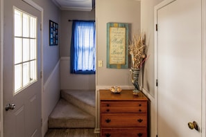 Un pasillo con un aparador de madera, un letrero decorativo y una ventana con cortinas.
