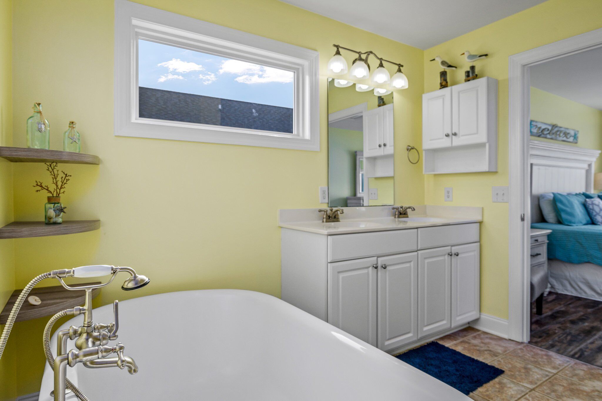 A bathroom with a bathtub, white cabinets, a window, and a mirror.