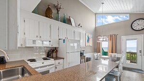 Una cocina moderna con armarios blancos, encimeras de granito y vista al océano a través de un ventanal corredera.