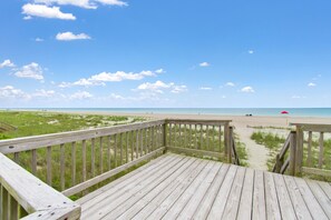 Une terrasse en bois qui mène à une plage, avec un ciel dégagé.