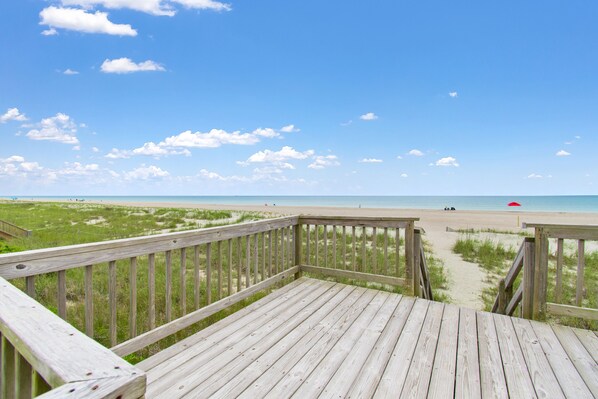 Una terraza de madera que da a una playa, bajo un cielo despejado.