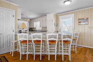 A kitchen with white cabinets, a dining table with four white chairs, and a window with blinds.