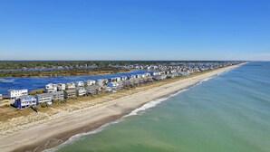 Zona residencial costera con propiedades frente al mar, una playa de arena y un cielo azul despejado.