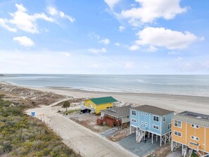 Um imóvel costeiro com vista para a praia, apresentando uma casa amarela com telhado verde, uma casa azul e uma casa amarela com telhado vermelho.