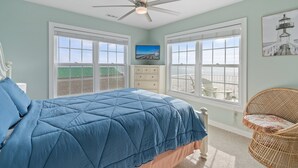 A bedroom with a bed, a ceiling fan, a dresser, and a wicker chair. - "Mocean Granted" - Oceanfront Home, 5 Bedrooms / 4 Bathrooms (Holden Beach)