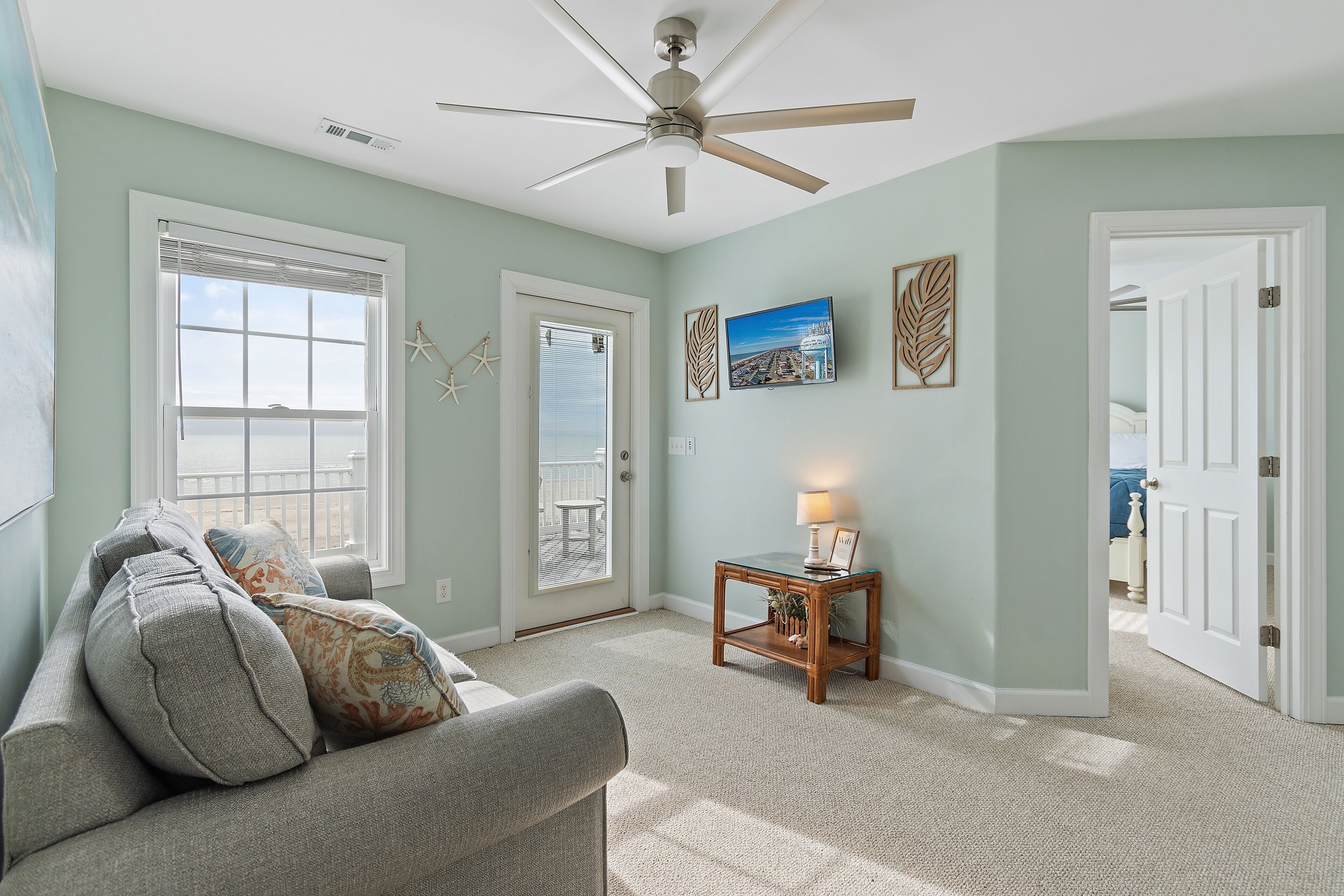A living room with a ceiling fan, a sofa, a coffee table, and a door leading to another room.