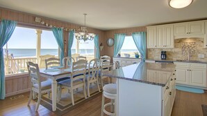 A kitchen with a view of the ocean, wooden flooring, white cabinets, and a dining area with chairs and a table. - "Goin' Coastal" - Oceanfront Home, 4 Bedrooms / 4.5 Bathrooms (Holden Beach)