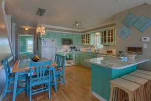 A kitchen with teal cabinets, a wooden dining table with chairs, and a central island with a marble countertop. - "Turtles Nest" - Oceanfront Duplex, 3 Bedrooms / 3 Bathrooms (Holden Beach)