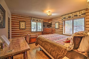 A log cabin-style bedroom with a wooden bed, a dresser, a desk, and framed pictures on the walls.
