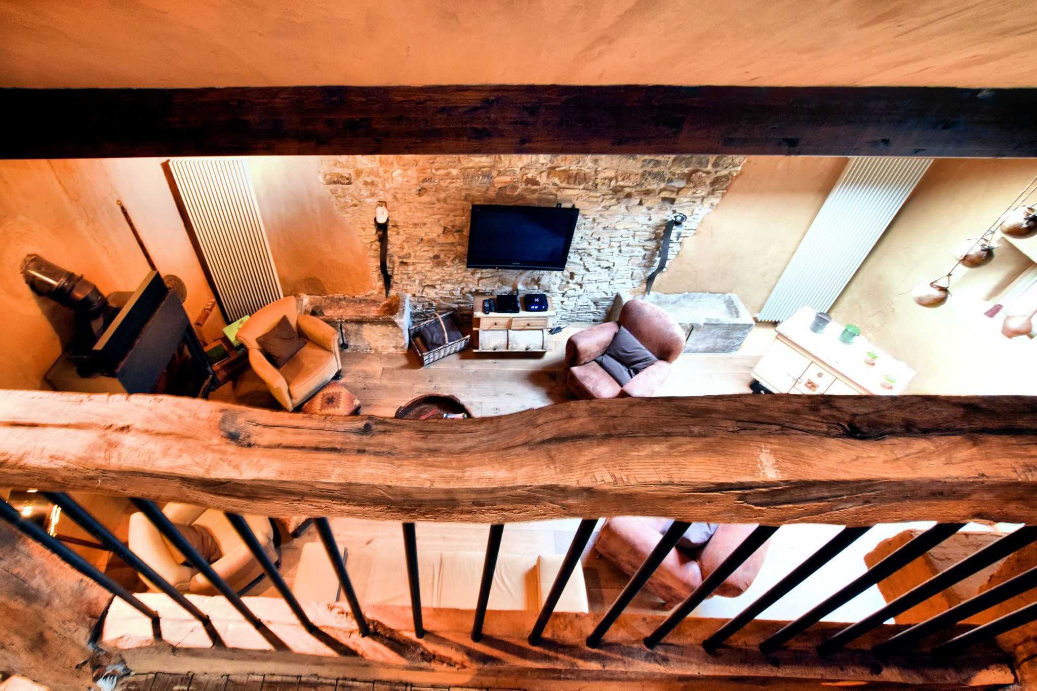 A rustic stone wall with a flat-screen TV, a wooden chair, and a sofa in a cozy living area.