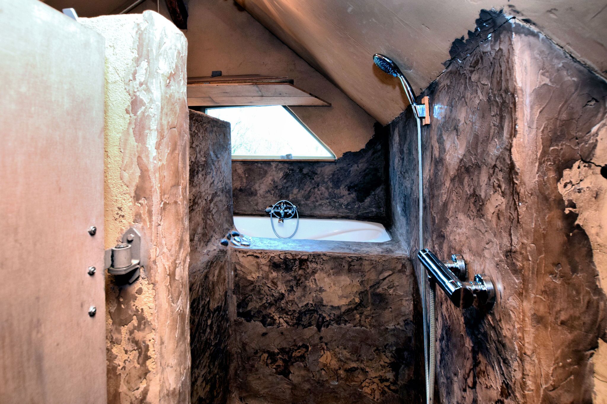 Een rustieke badkamer met een stenen muur, een klein raam en een douche.