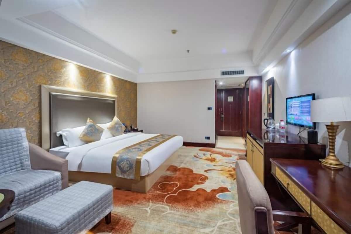 A hotel room with a large bed, a desk, a chair, and a television.