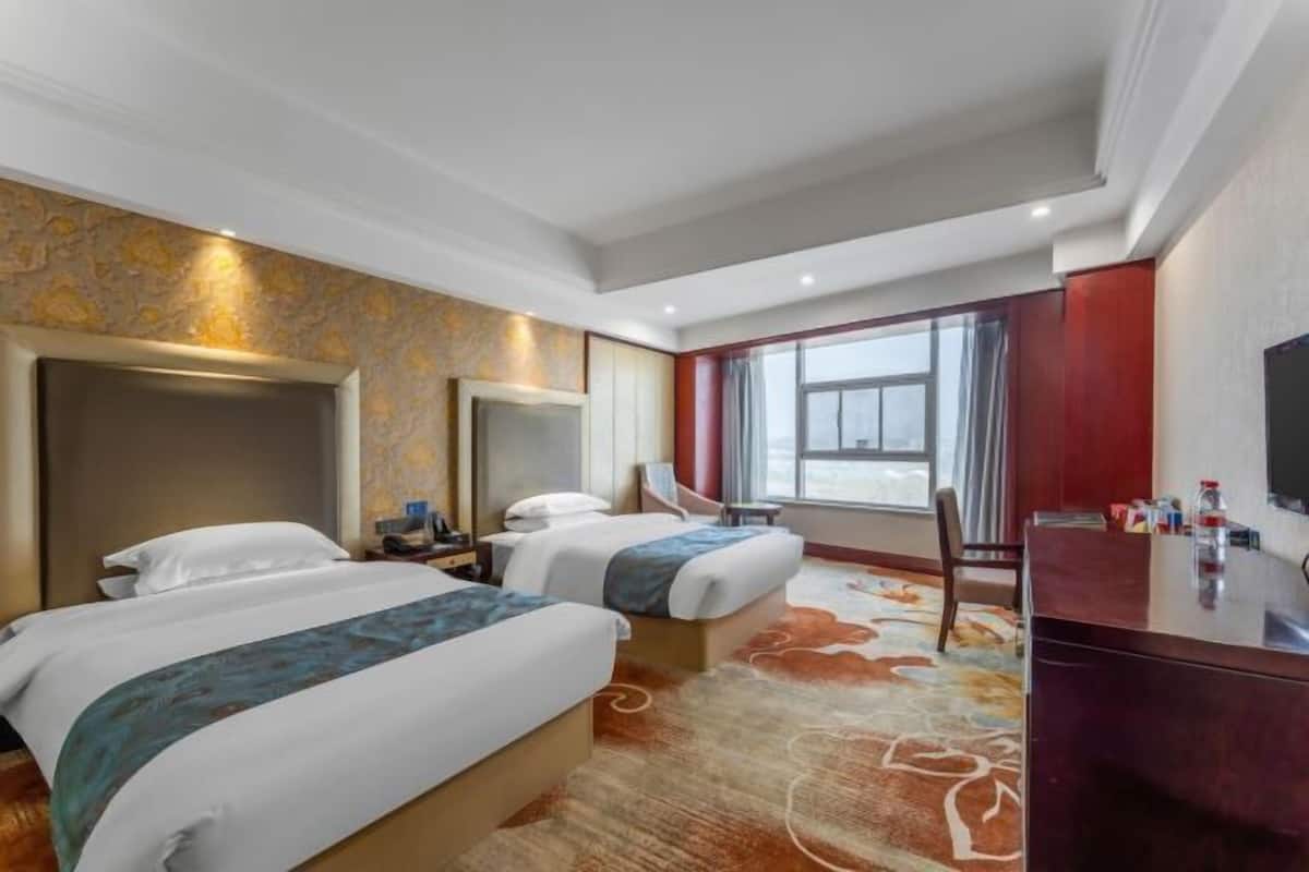 A hotel room with two beds, a large mirror, a desk with a chair, and a window with curtains.