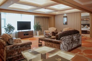A spacious living room with a large flat-screen TV, plush seating, and a large window. - Hanjiang International Hotel (Danjiangkou)
