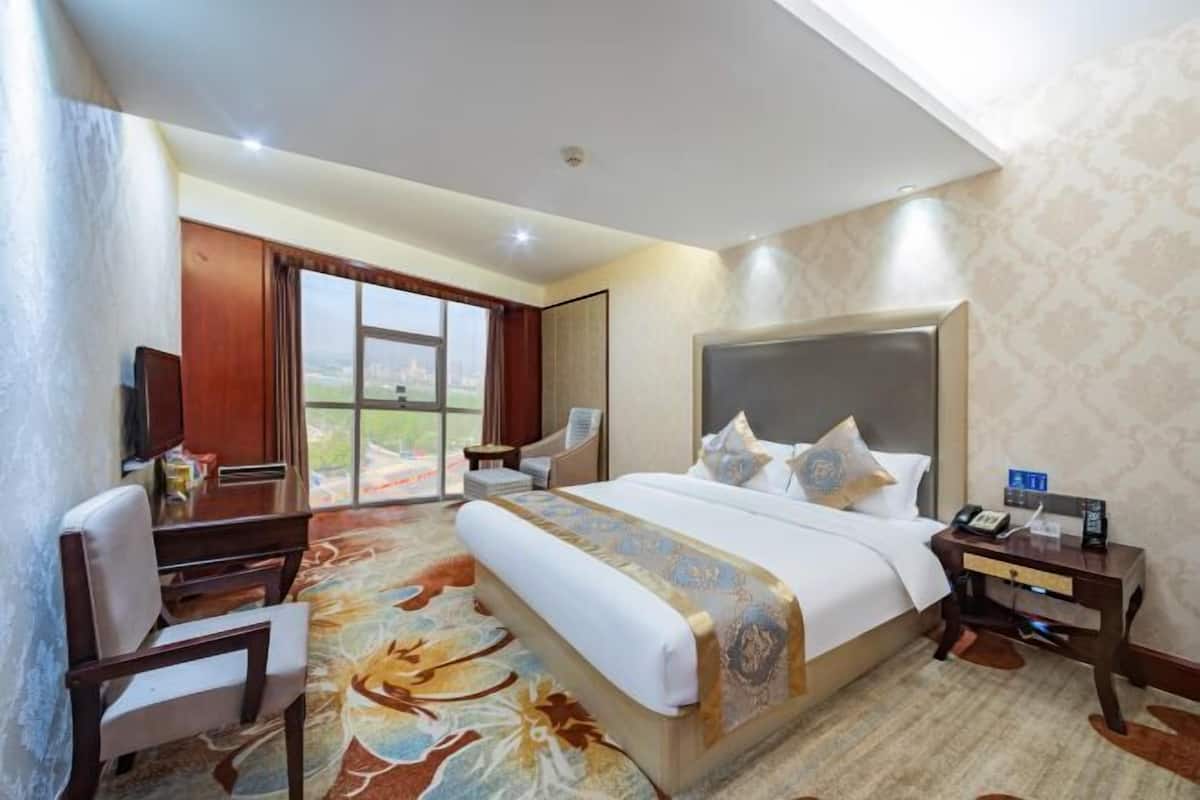 A hotel room with a large bed, a desk, a chair, and a view of the outdoors.