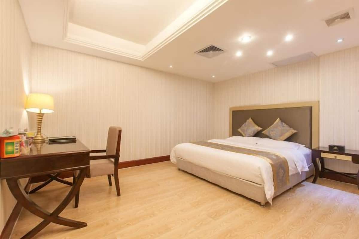 A hotel room with a bed, a desk, a chair, and a lamp.