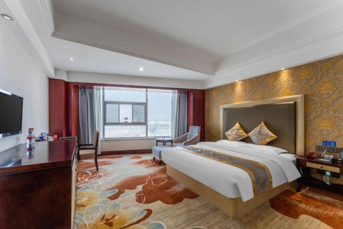 A hotel room with a large bed, a desk, a chair, and a TV.