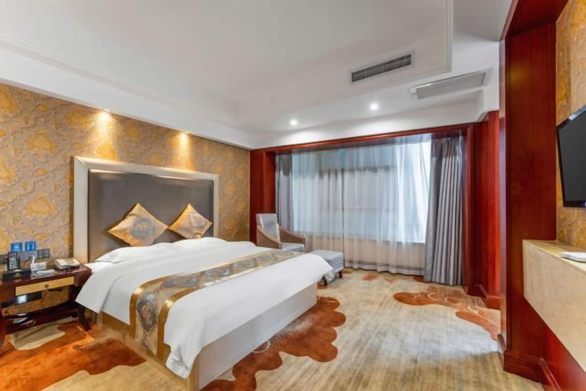 A hotel room with a large bed, a desk with a telephone, a chair, and a television.