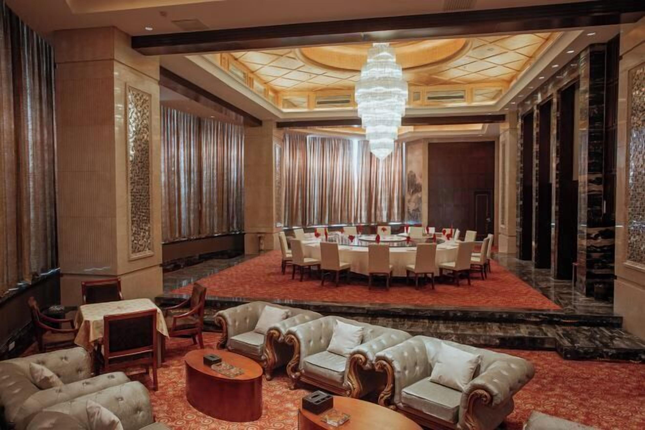 A spacious lobby with a round table and chairs, leather sofas, and a chandelier.