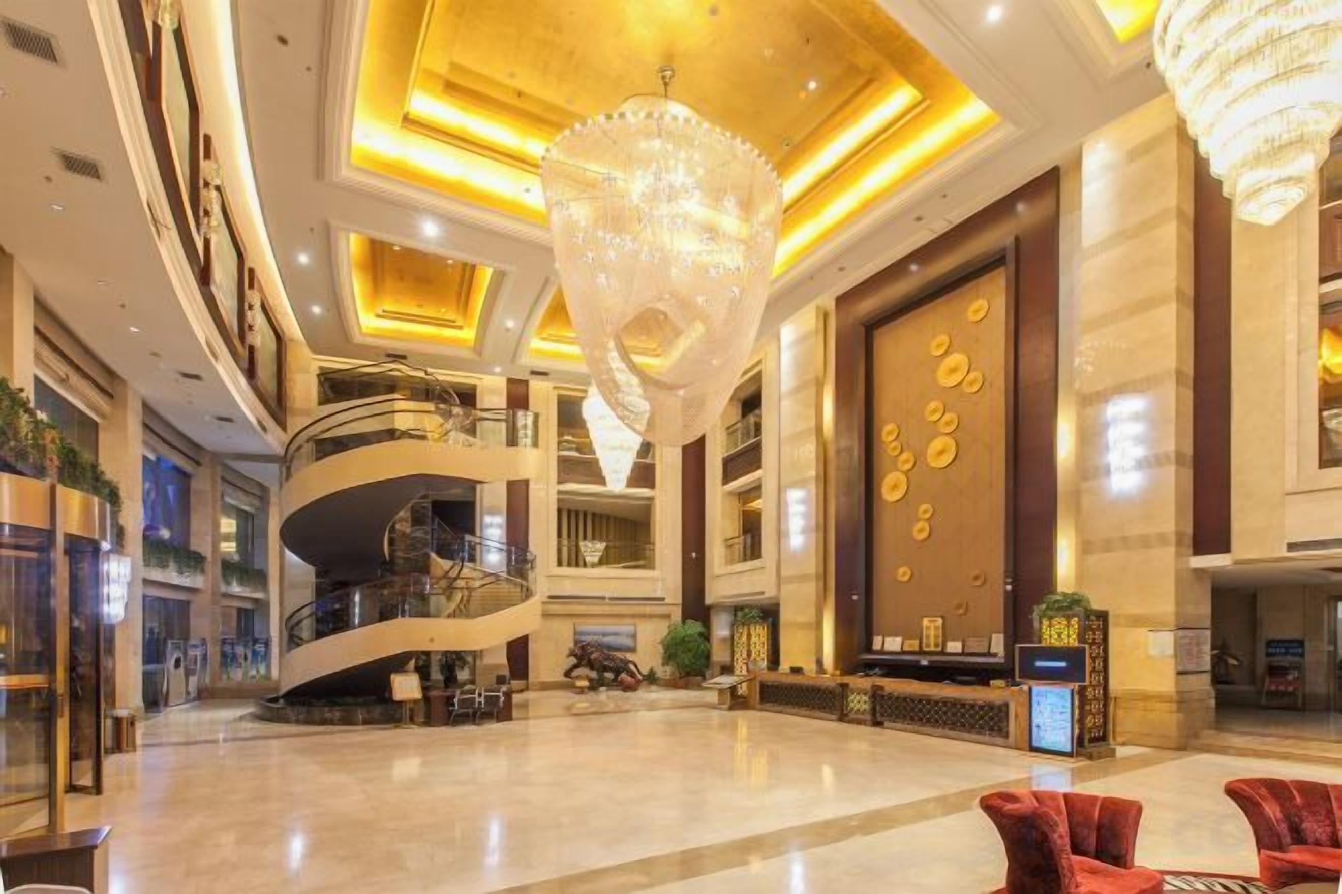 A spacious lobby with a grand chandelier, a spiral staircase, and a large reception desk.